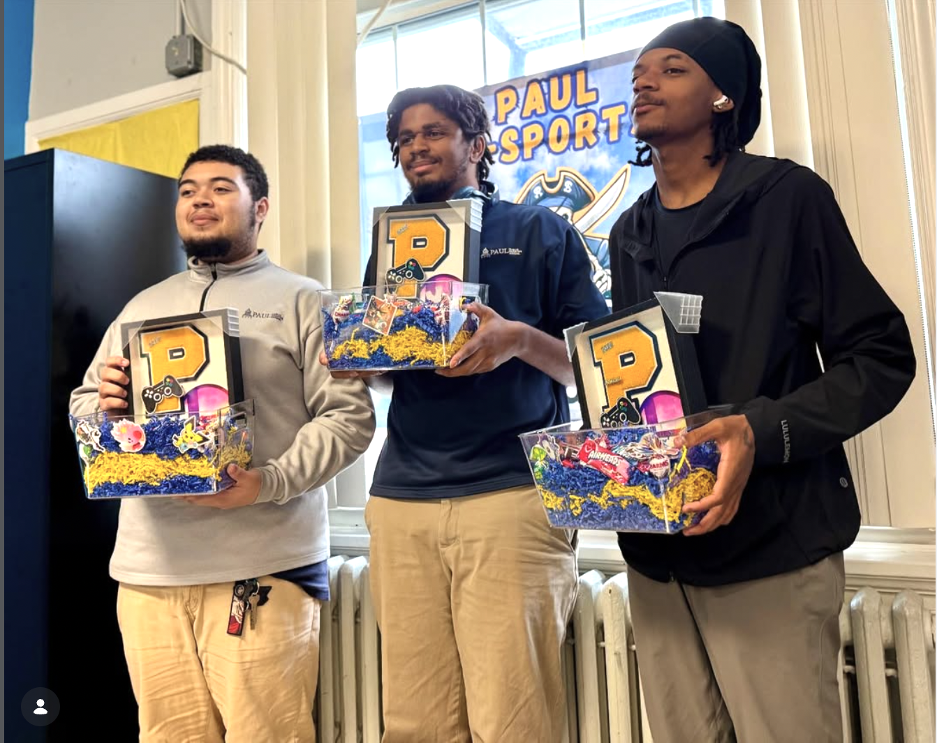 Three Paul International esports competitors holding Pirate-branded prize baskets in front of a Paul E-Sports banner